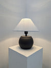 black Table lamp with a black base and white shade on a white pedestal against a light gray wall.