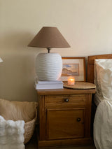 Cream cheese terracotta lamp softly lit beside upholstered chair

